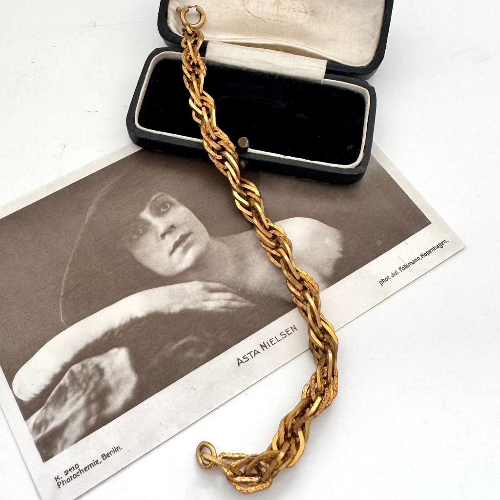 A thick gold chain bracelet with a lobster clasp, draped over an open black jewelry box and a vintage black-and-white photograph card featuring the name Asta Wilson.