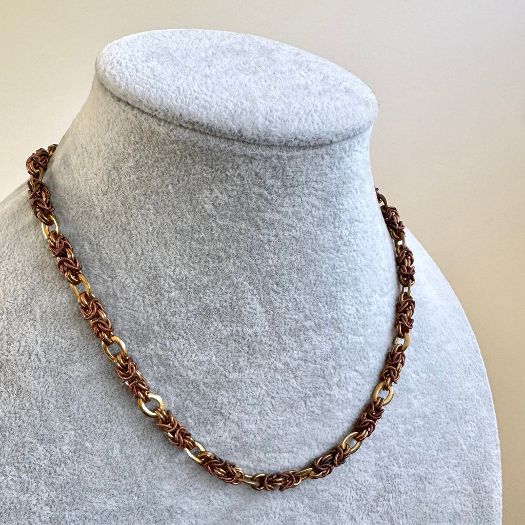A close-up of a Jakob Bengel Byzantine link necklace displayed on a light gray fabric jewelry bust against a plain beige background.