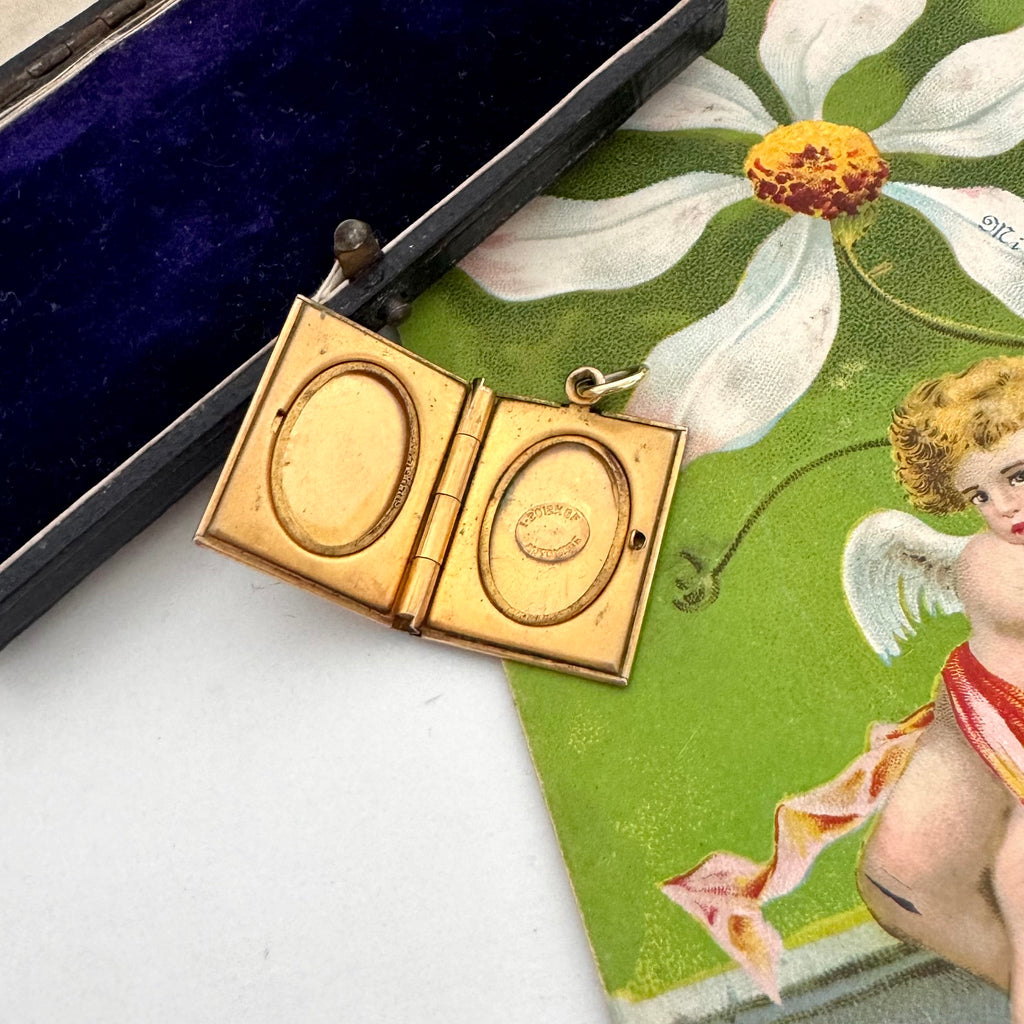 Gold locket on a decorative card with floral and cherub design