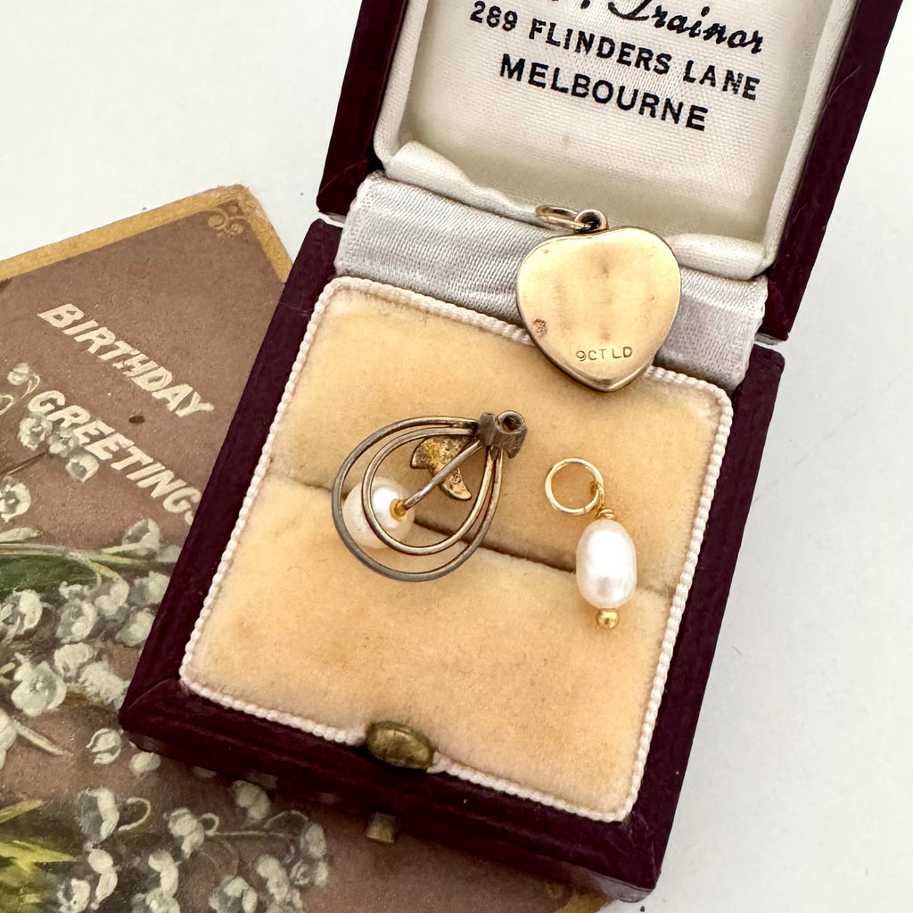 Jewelry box with gold heart pendant, gold and pearl pendant and a pearl in an open jewellery box