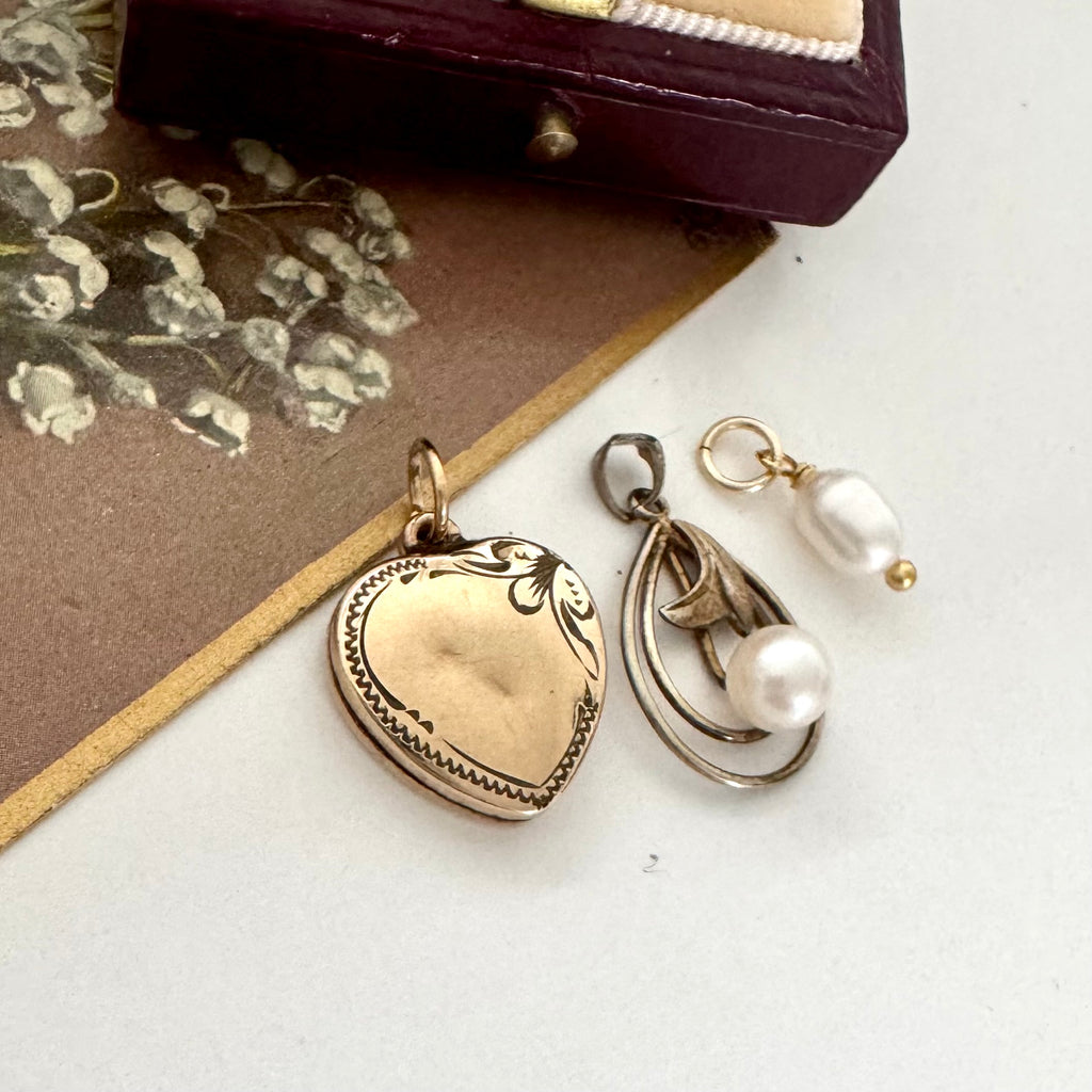 Vintage gold heart-shaped locket, pearl pendant and pearl on a white surface.