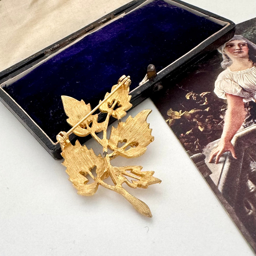Vintage gold leaf brooch in a decorative box with an image of a woman on the side.