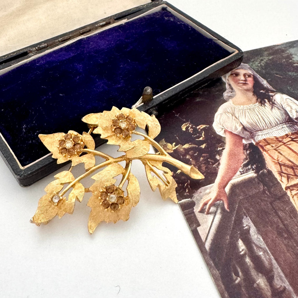 Vintage gold tone floral brooch with a vintage-style box and image in the background