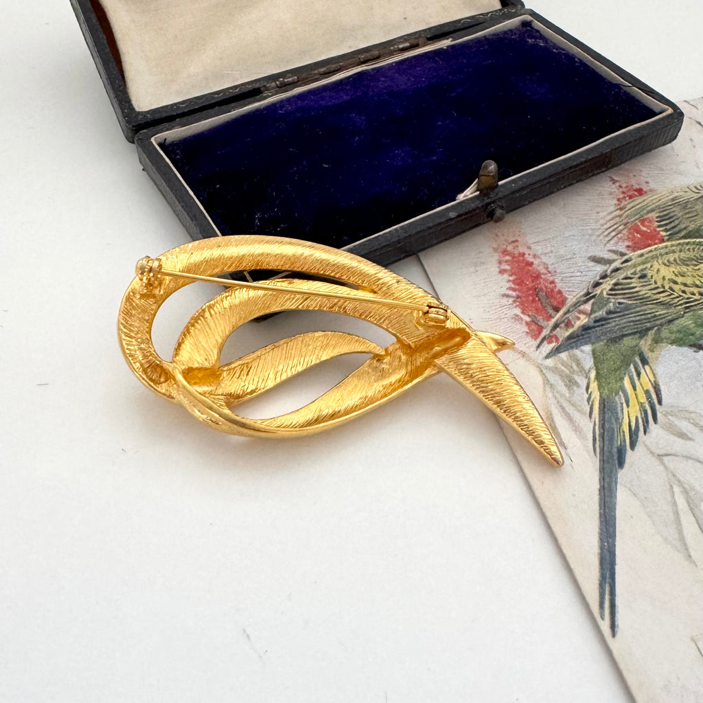 Gold brooch on a white surface with a decorative box in the background