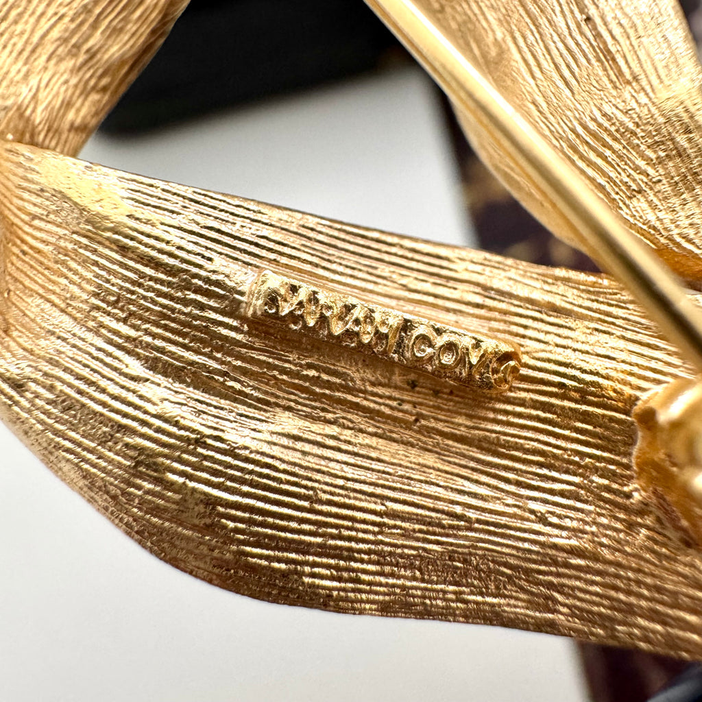 Close-up of a gold brooch with 'Sarah Coventry' branding on a white background