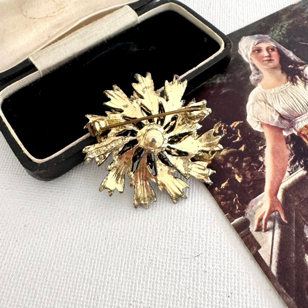 Back of vintage signed Hollywood gold tone flower brooch on an old jewellery box and with a vintage postcard