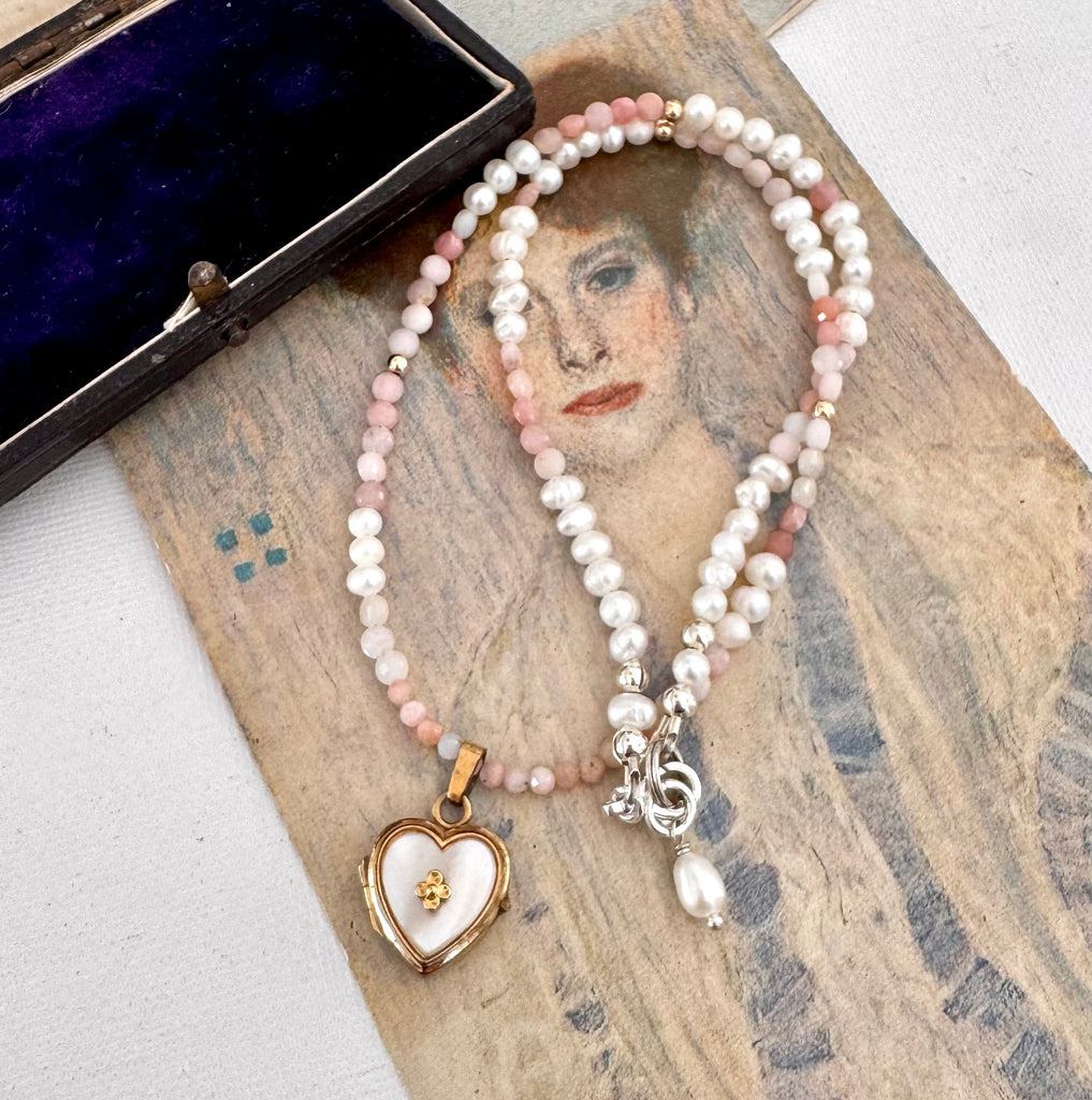 vintage heart locket and pearl and peruvian opal necklace on an open jewellery box and with a vintage postcard.