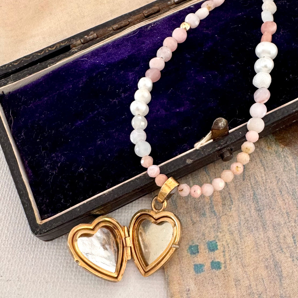 vintage heart locket and pearl and peruvian opal necklace on an open jewellery box and with a vintage postcard.