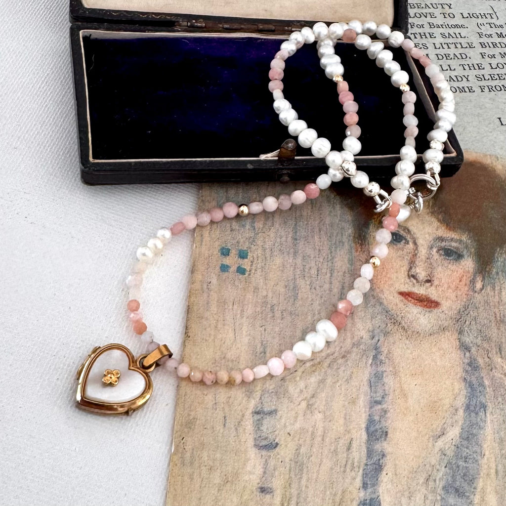 vintage heart locket and pearl and peruvian opal necklace on an open jewellery box and with a vintage postcard.