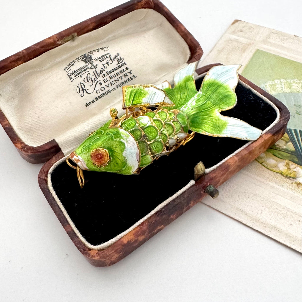 A vintage Koi fish pendant with green enamel scales and gold-toned metal details, displayed inside an open antique presentation box with a black velvet lining.