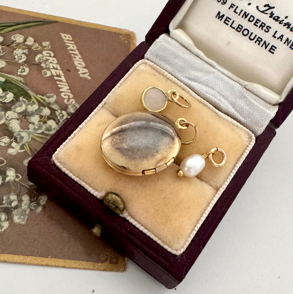 Gold jewelry set with a locket and pearl pendant in an open jewelry box.