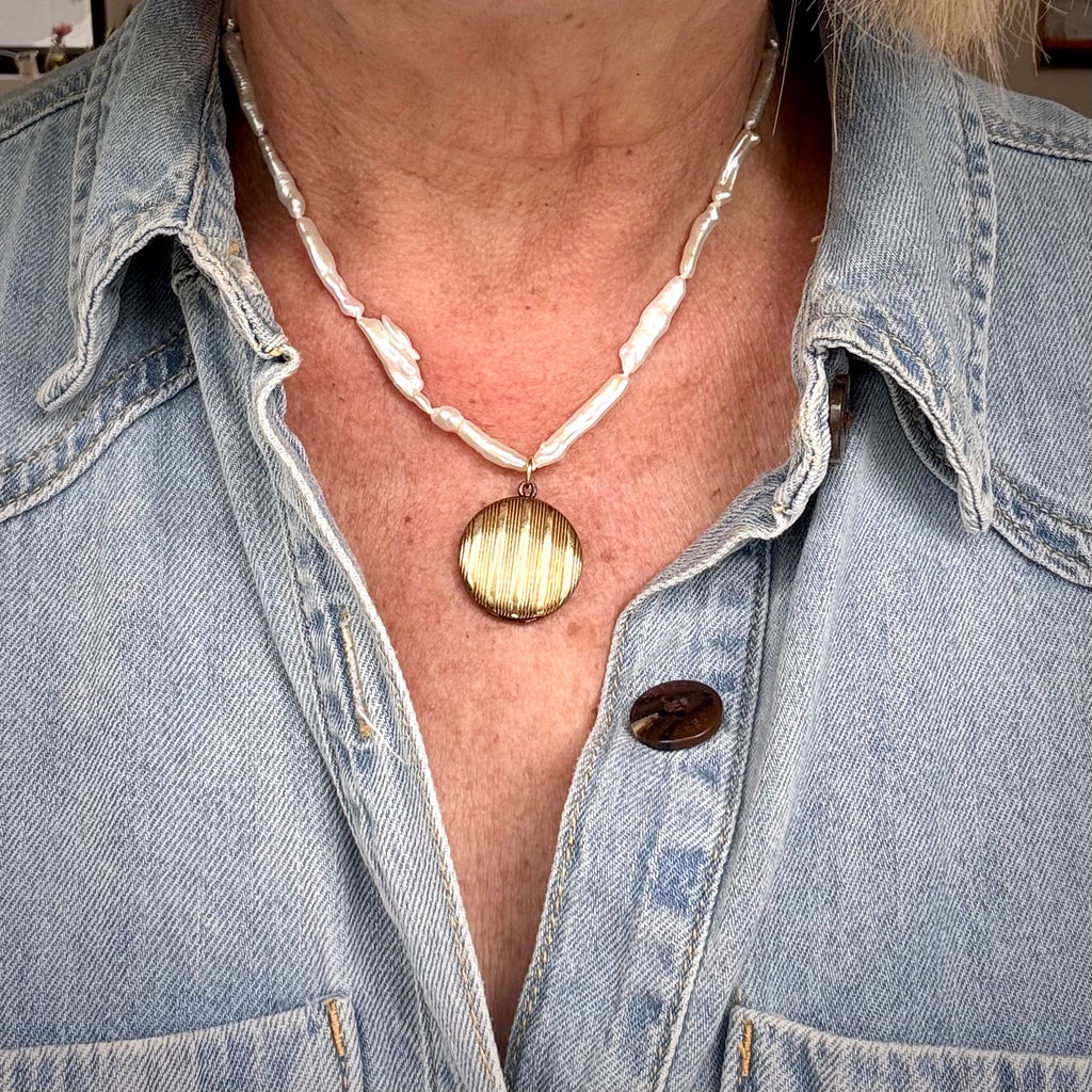 Person wearing a denim jacket with a necklace featuring a round pendant.