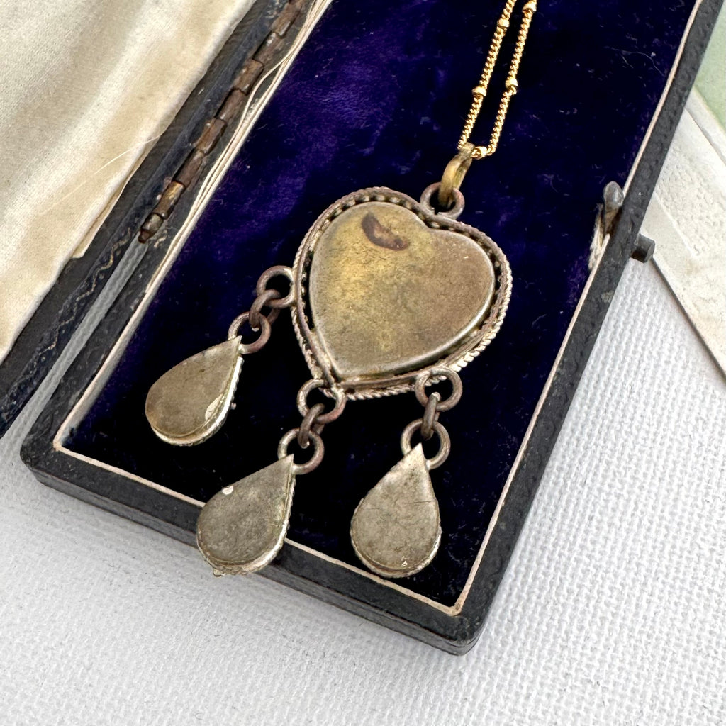 The back of a vintage micro moasic pendant and three dangling teardrop charms, displayed inside an open black velvet jewelry box.