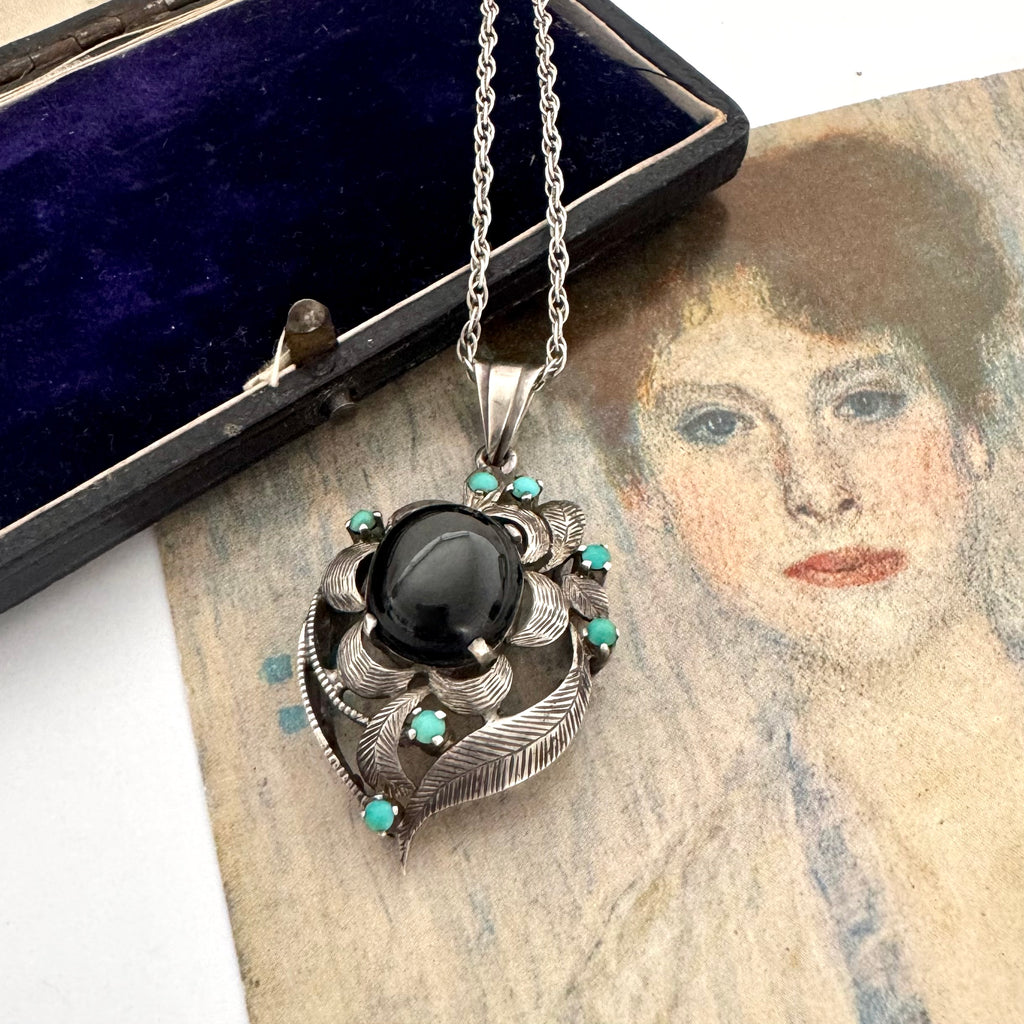 Vintage art nouveau mid century revival necklace with black stone and turquoise stones on a textured surface