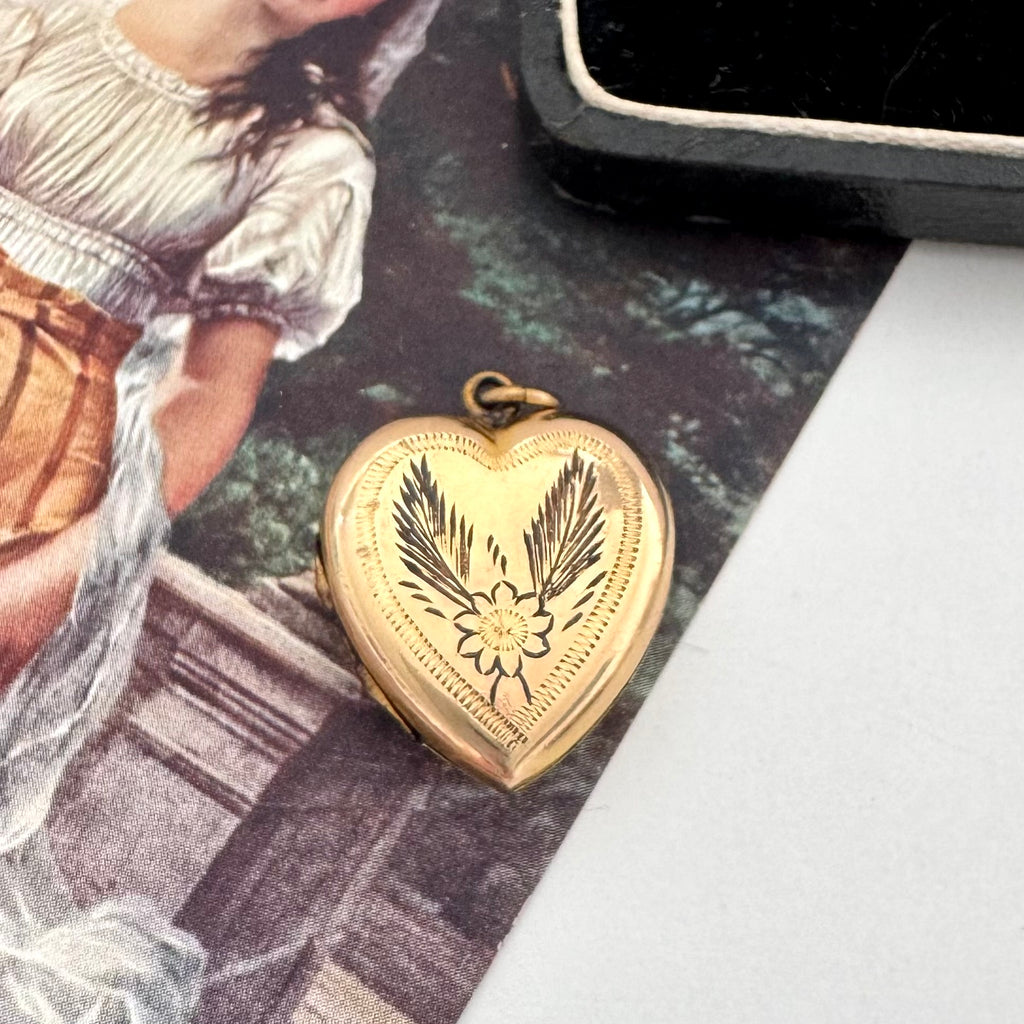 Gold heart-shaped locket with floral design on a textured surface