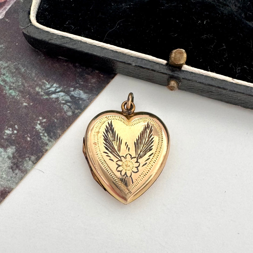 Gold heart-shaped locket with floral design on a white surface