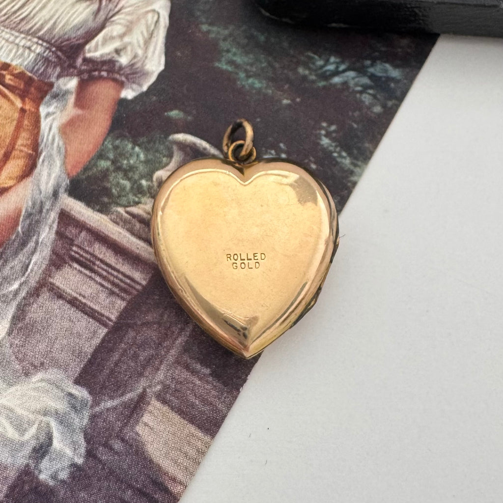 Gold heart-shaped locket with 'Rolled Gold' engraving on a textured surface.