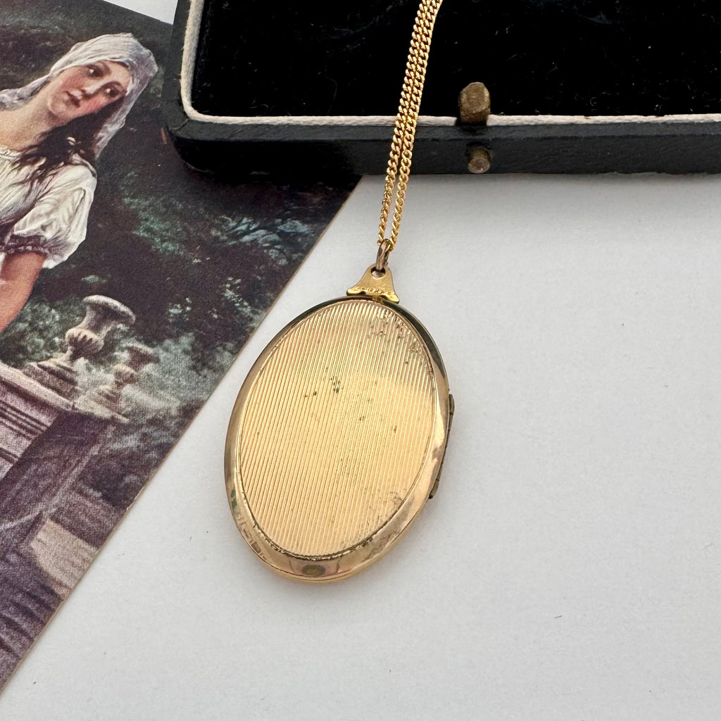 Gold locket on a white surface with a vintage-style card in the background