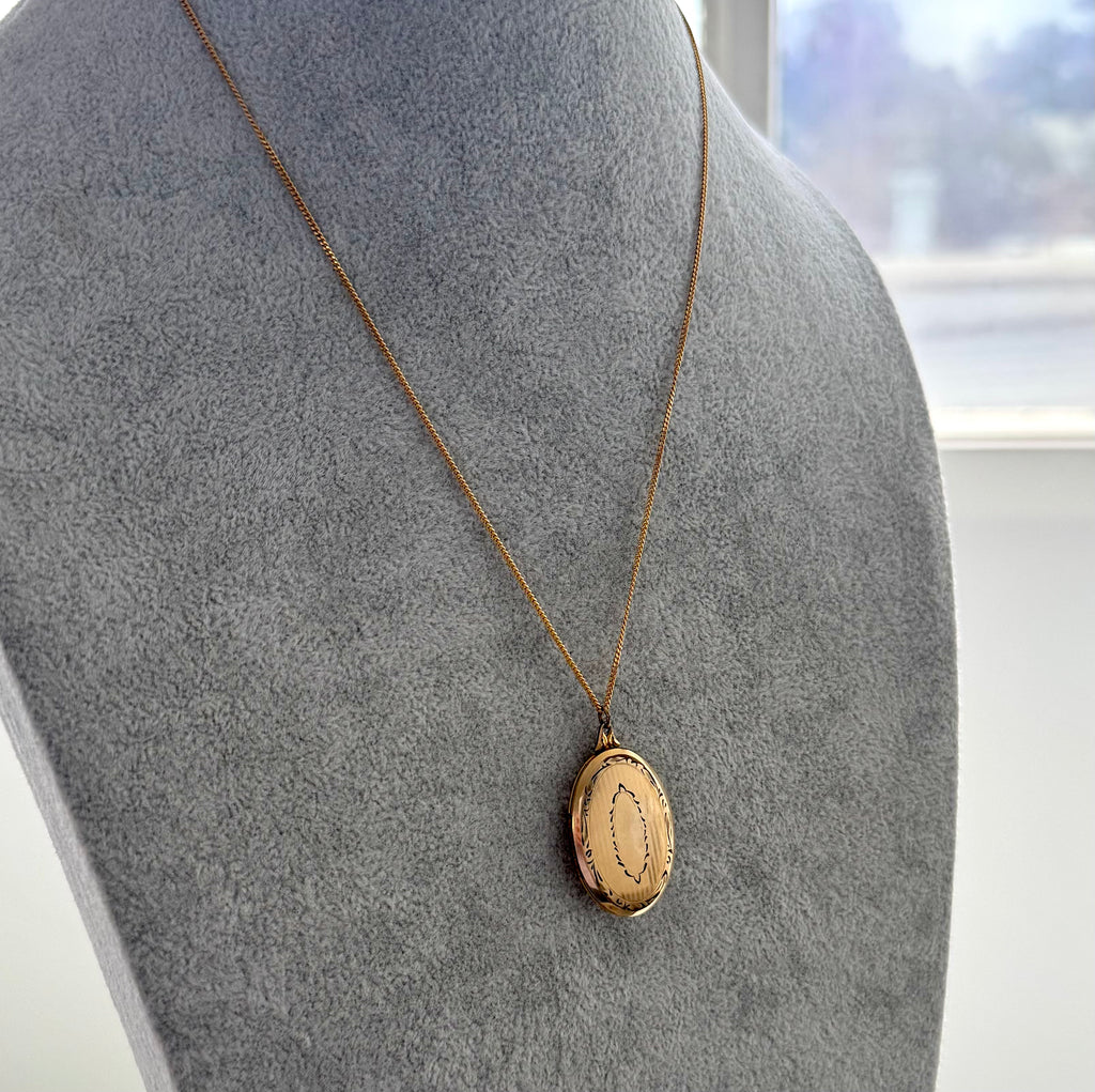 Vintage gold locket necklace with a pendant on a mannequin bust against a neutral background