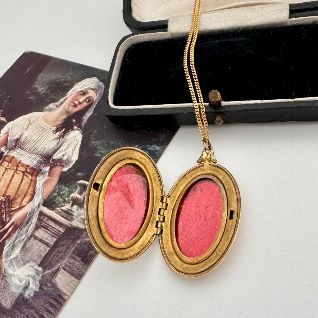 Vintage gold locket with pink interior on a white surface with an open box in the background.
