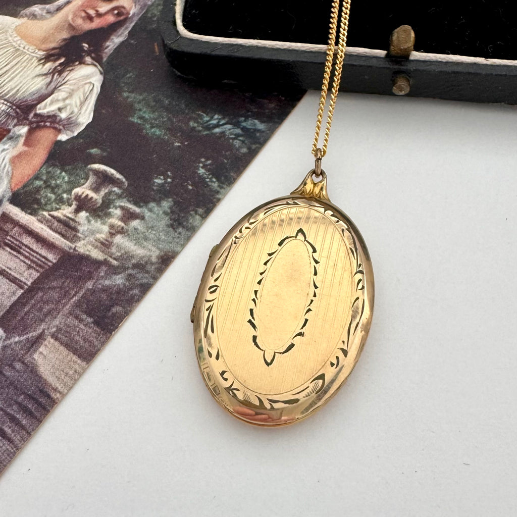 Vintage rolled gold locket on a white background with a vintage postcard
