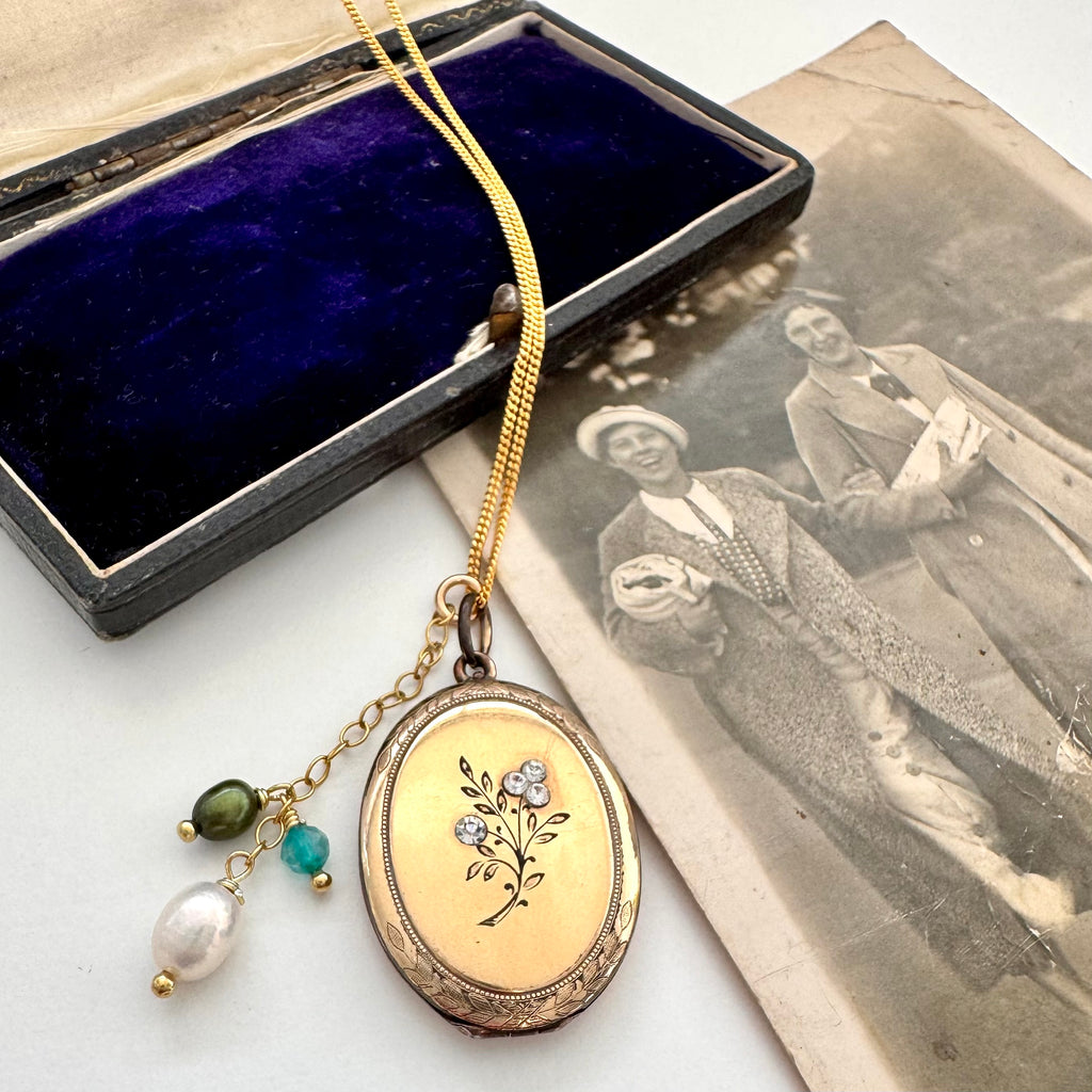 Vintage gold locket with floral design on a white surface with an old photograph.