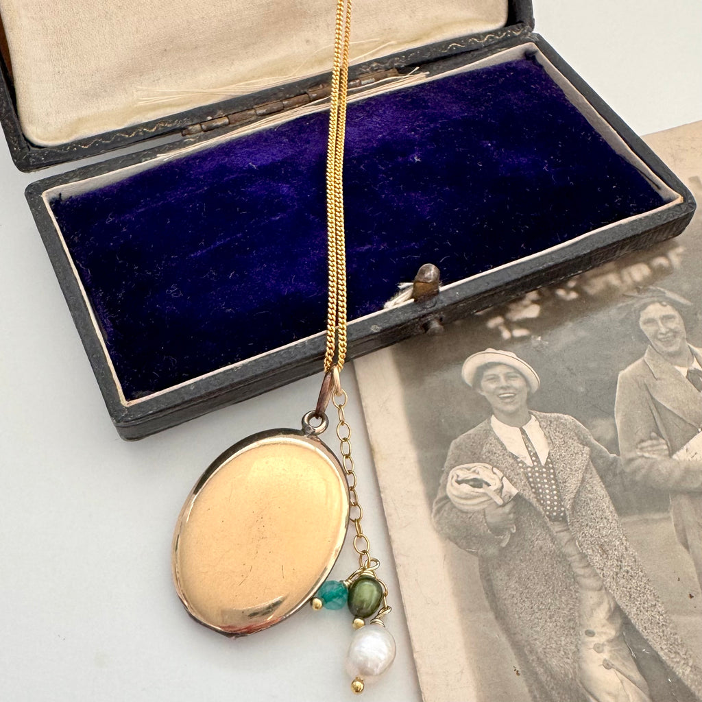 Gold locket with pendant on a chain next to an open jewelry box and vintage photograph.