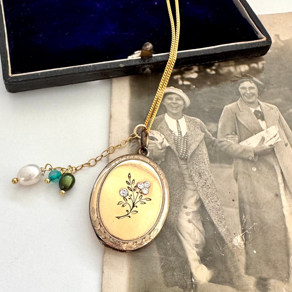 Vintage locket with floral design on a white surface with an old photograph in the background.
