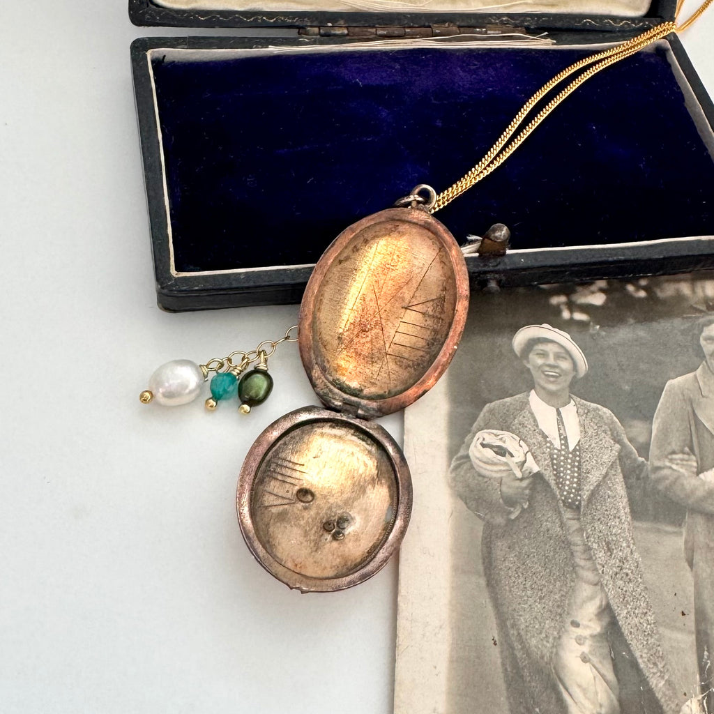 Vintage locket with decorative chain on a white surface next to an old photograph.