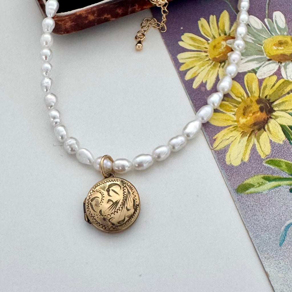 Vintage rolled gold locket and pearl necklace on a vintage postcard and jewellery box