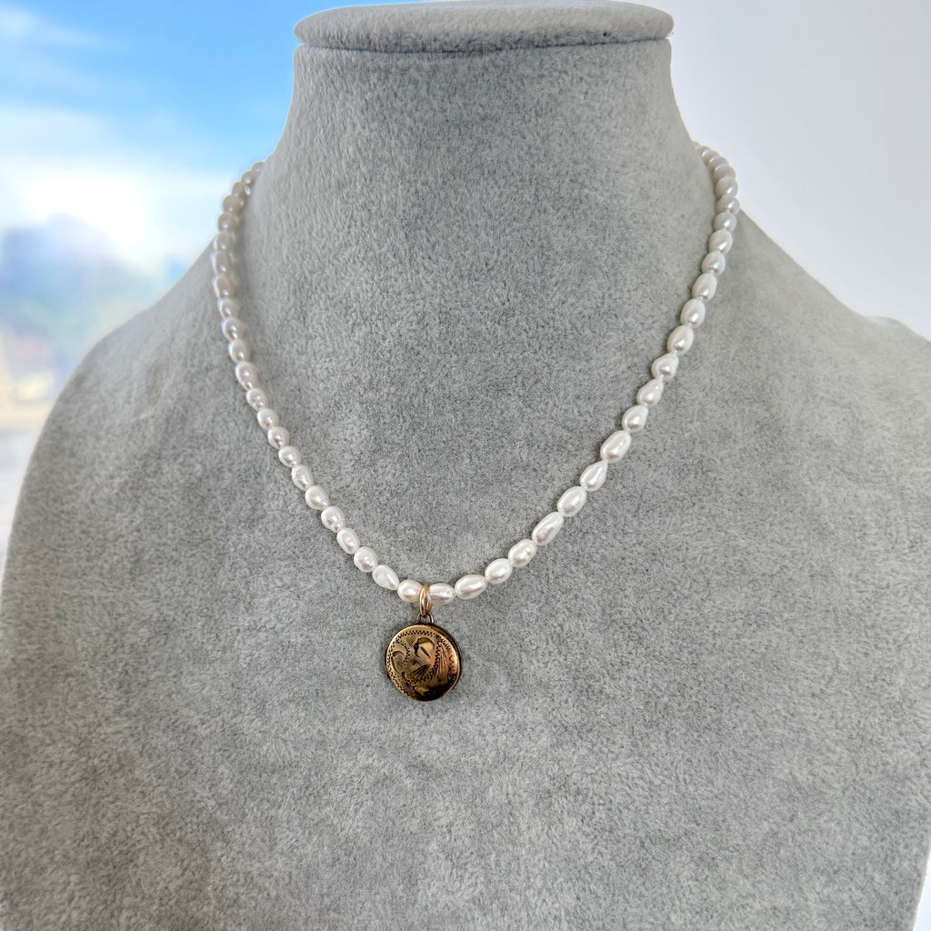 Vintage rolled gold locket and pearl necklace on a grey jewellery bust