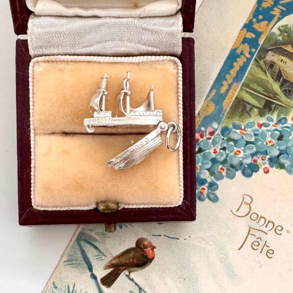 Vintage silver Mayflower ship charm in a jewelry box with a vintage card in the background