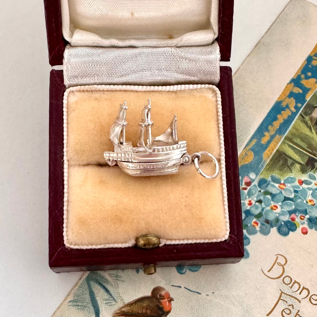 Vintage silver Mayflower ship charm in a jewelry box with a vintage card in the background