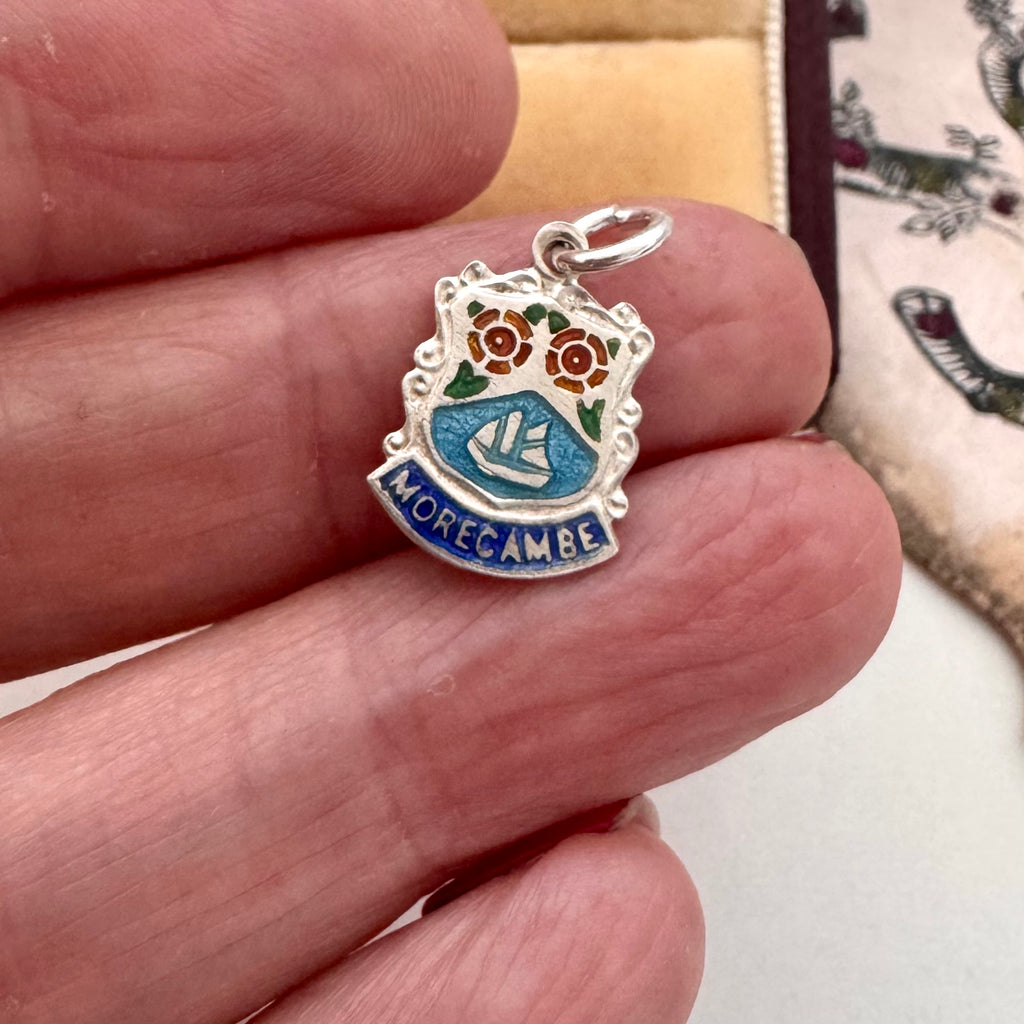 Silver pendant with floral design and 'Morecambe' text held between fingers