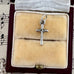 Silver crucifix charm on a beige cushion in a jewelry box with music sheet background