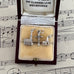 Three silver charms in a jewelry box with sheet music in the background