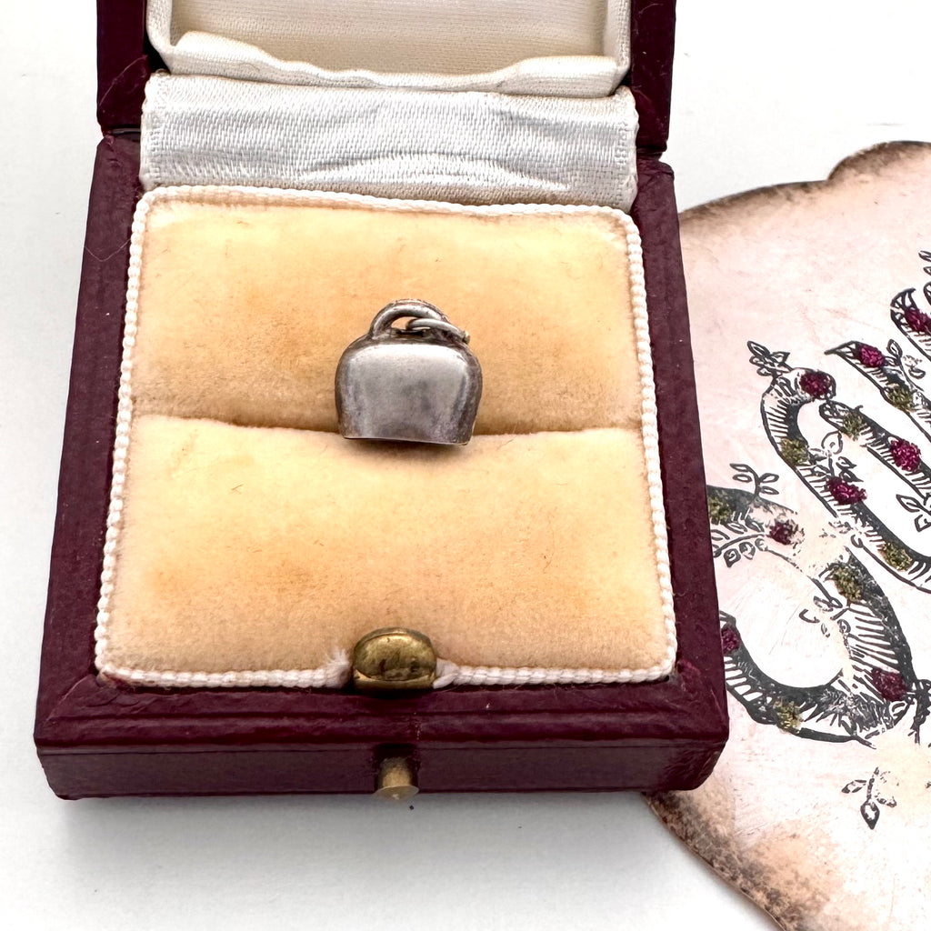 Silver bell charm in a jewelry box with a decorative card in the background