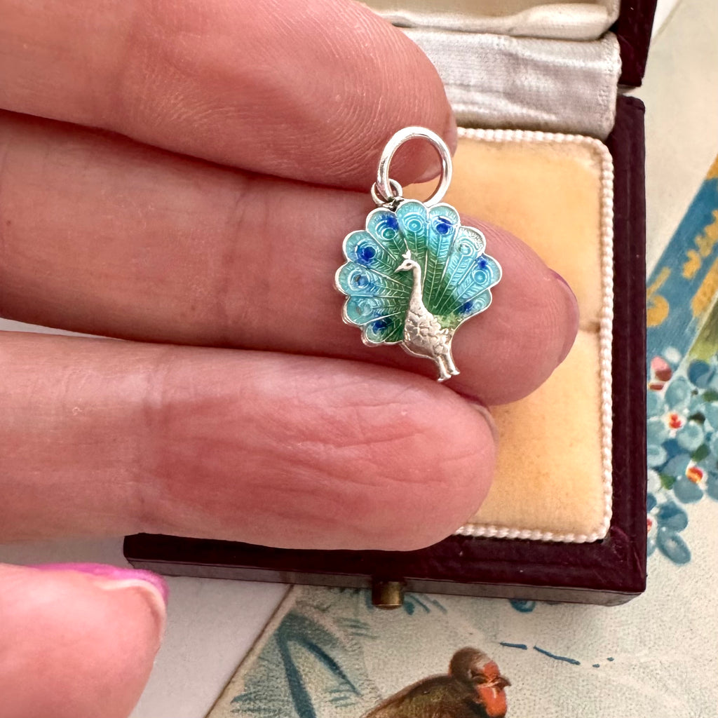 Vintage silver and enamel peacock charm in a woman's hand