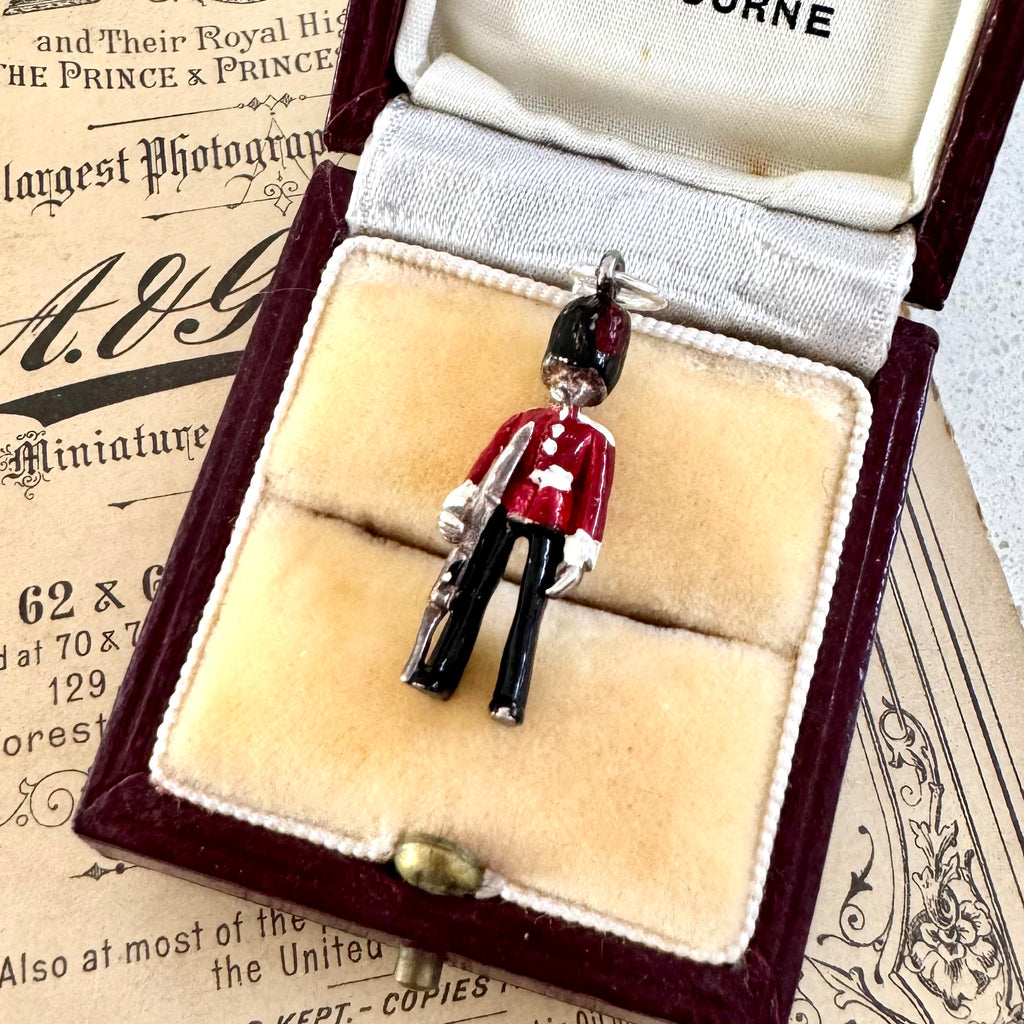 Vintage silver and enamel British Royal Foot Guard charm on display in an open jewelry box with vintage paper in the background.