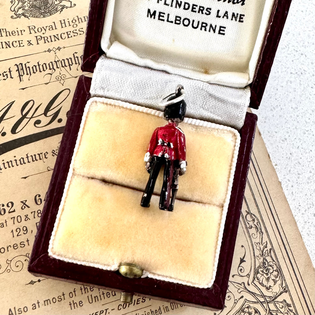 Vintage silver and enamel British Royal Foot Guard charm on display in an open jewelry box with vintage paper in the background.