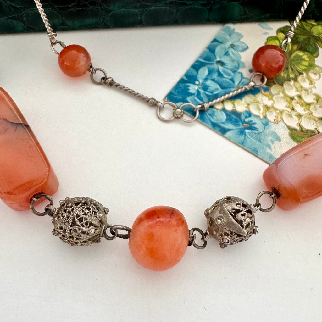 Vintage Middle eastern necklace with orange beads and silver filigree elements on a white surface