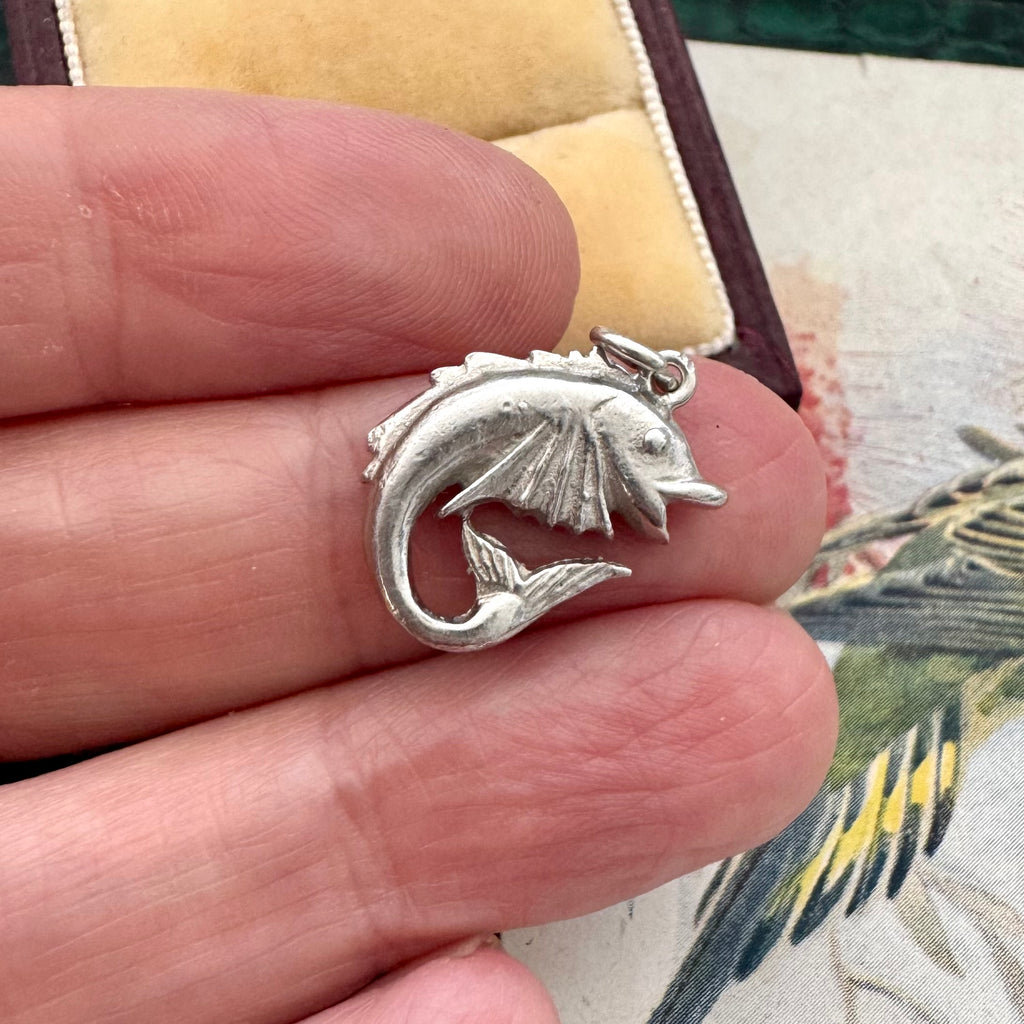 Vintage silver fish charm held between fingers with a floral background