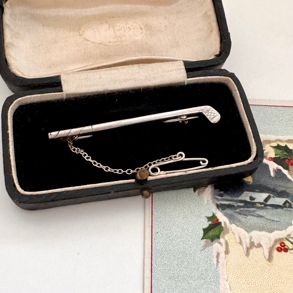 Vintage silver golf club brooch in an open jewelry box with a decorative card in the background