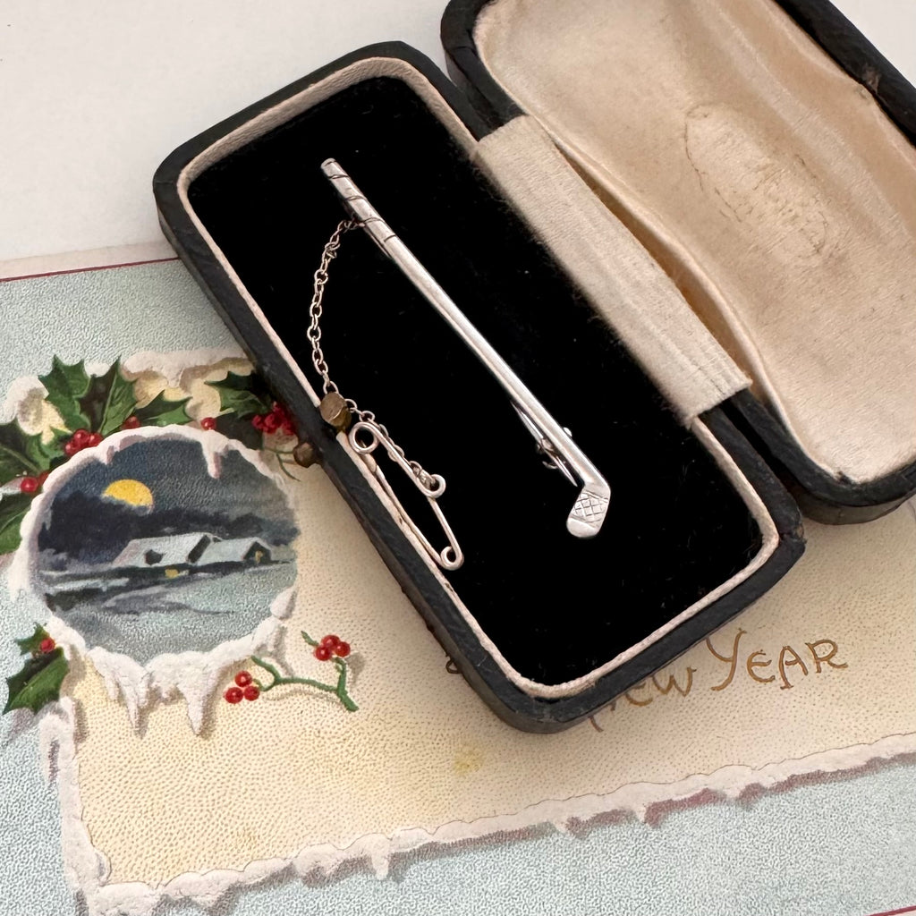 Vintage silver golf club brooch in an open jewelry box with a decorative card in the background