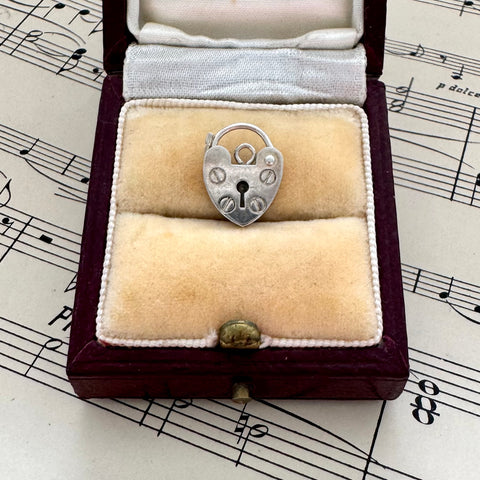 Silver heart-shaped lock pendant in a jewelry box on sheet music
