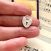 Silver heart-shaped lock charm held between fingers on a sheet of music.