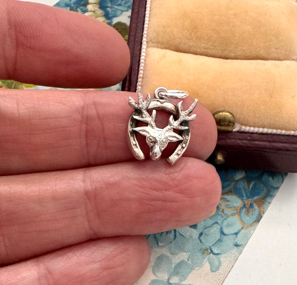 Silver horseshoe and stag charm held between fingers with a patterned fabric background