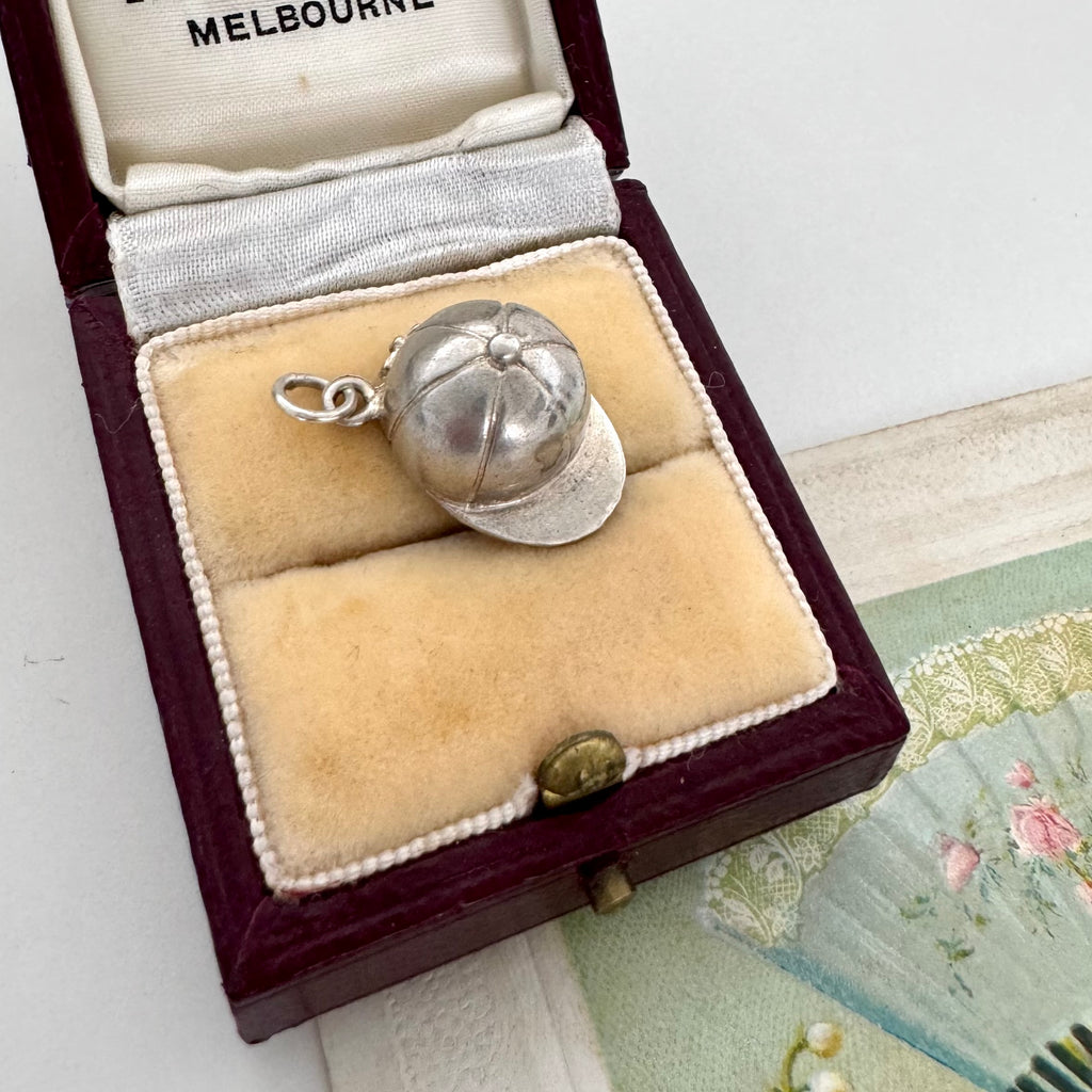 Vintage silver jockey cap charm/pendant in a jewelry box on a textured surface