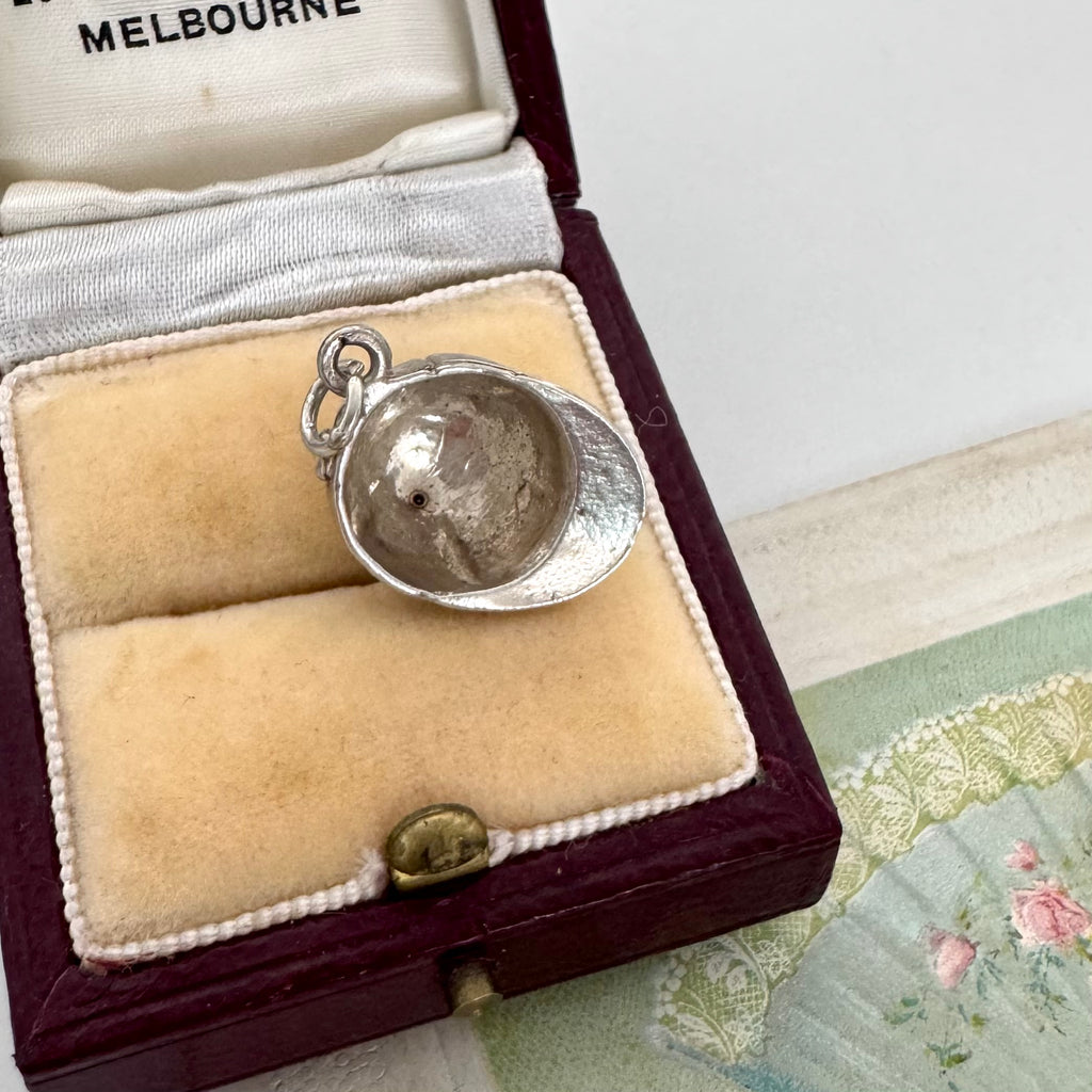 Vintage silver jockey cap charm/pendant in a jewelry box on a textured surface