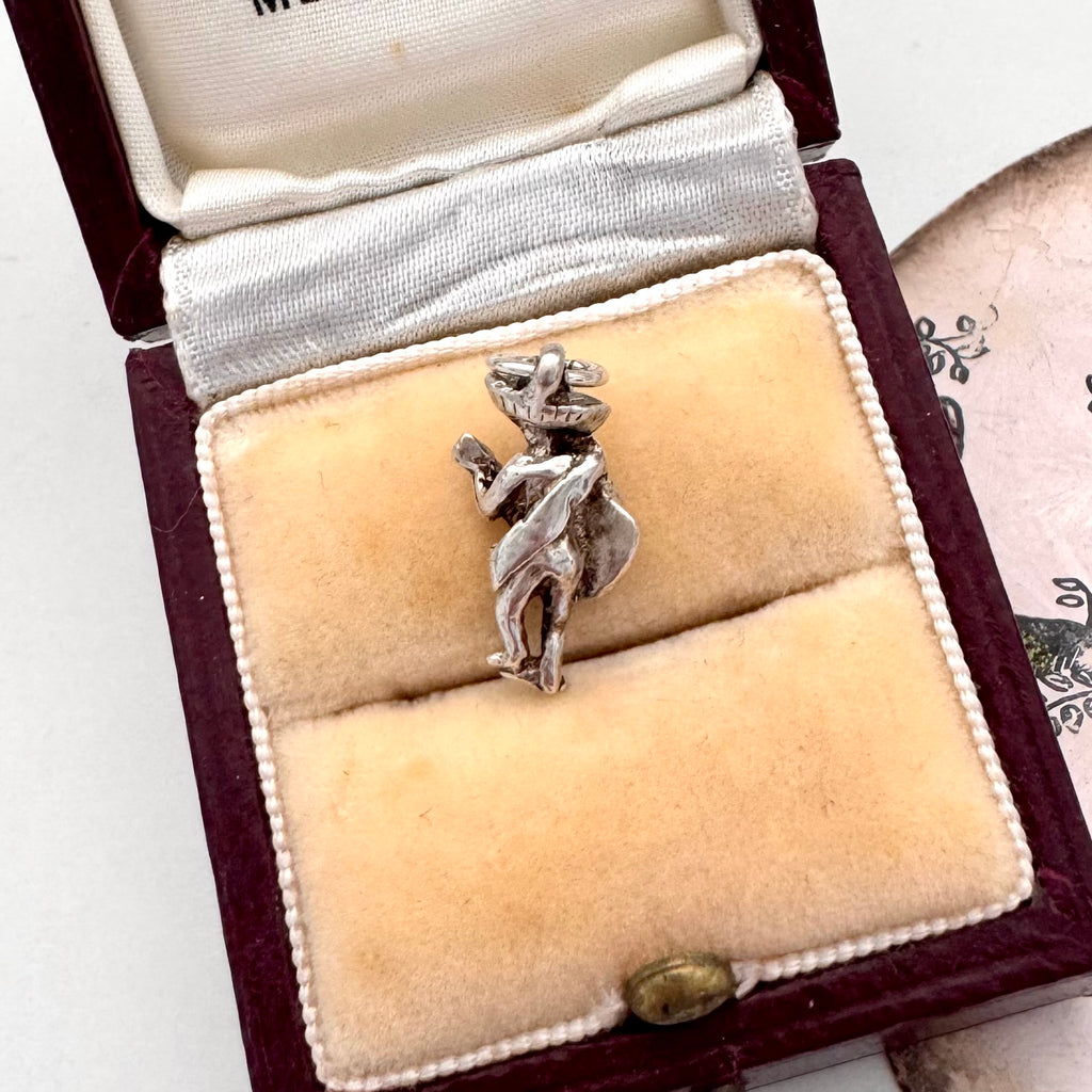 Vintage silver Mexican guitar player charm in a jewelry box with a decorative background